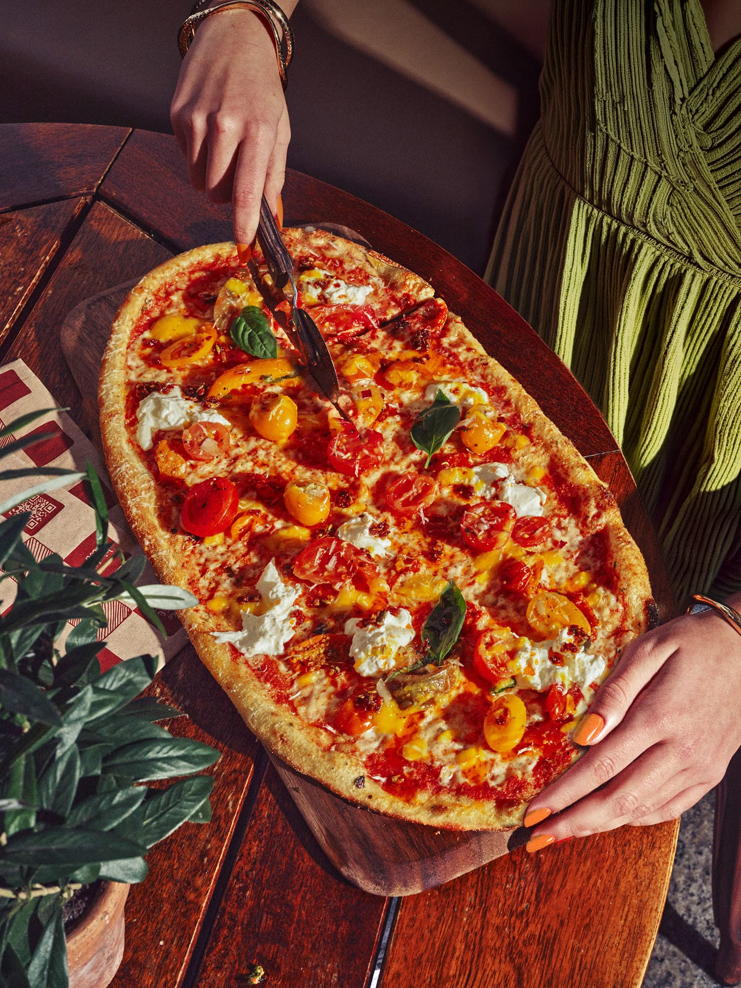Hands slicing rectangular pizza with colorful toppings