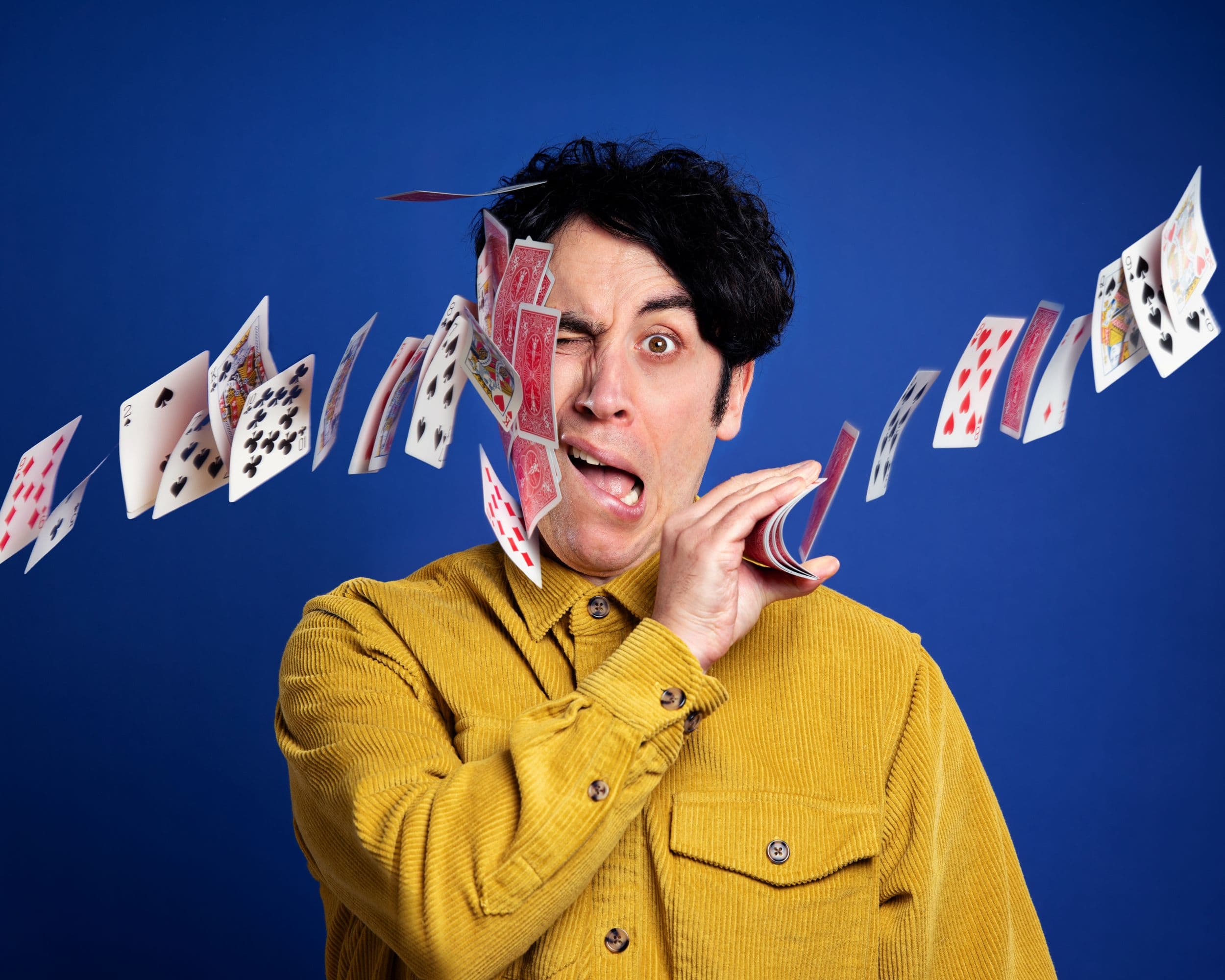 Pete Firman in yellow shirt performing card trick against blue backdrop