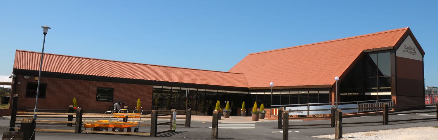 Modern brick garden center with large windows, red-tiled roof, and landscaped entrance under a clear blue sky.