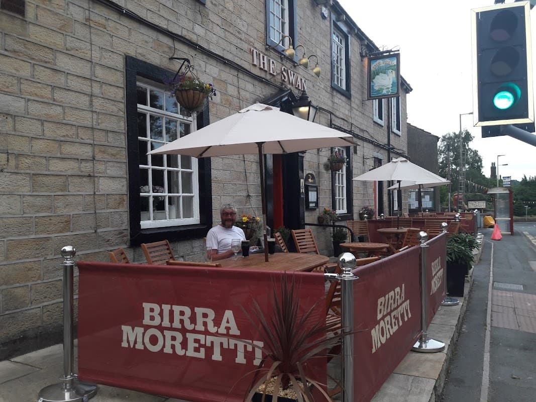 Quaint pub with outdoor seating, umbrellas, and a "Birra Moretti" banner, set in a stone building in Addingham.