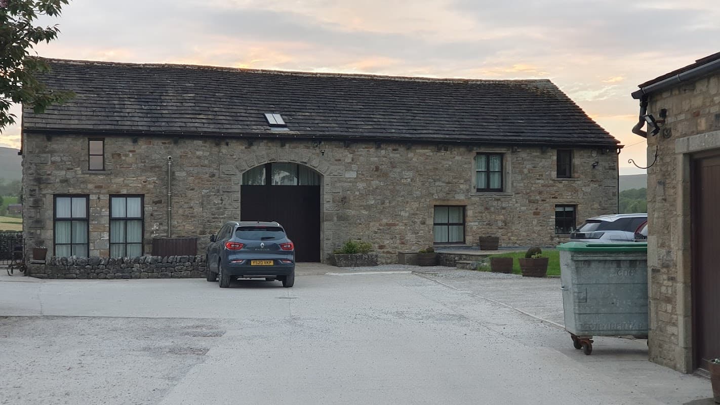 Stone cottage with a slate roof, parked cars, and a green bin, set in a rural landscape at Town End Farm, Yorkshire.