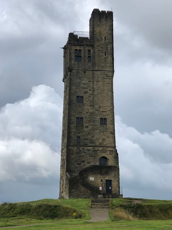 Tall stone tower atop a grassy hill under a cloudy sky, with steps leading to the entrance.