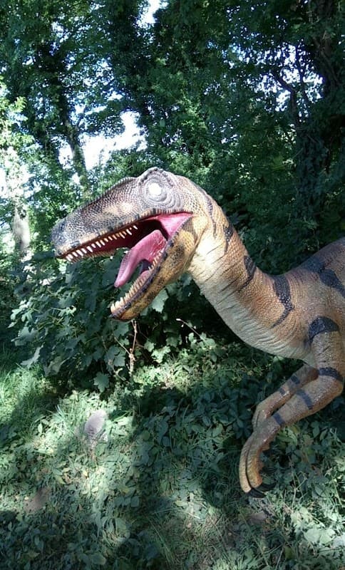 A large, realistic dinosaur sculpture among lush greenery, showcasing vibrant colors and intricate details.