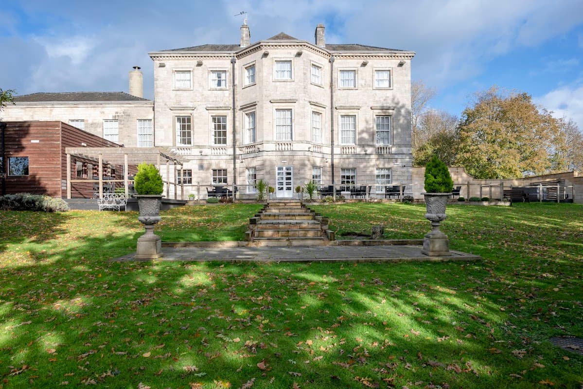 Aston Hall Hotel features a grand stone facade, manicured lawns, and decorative planters under a blue sky.