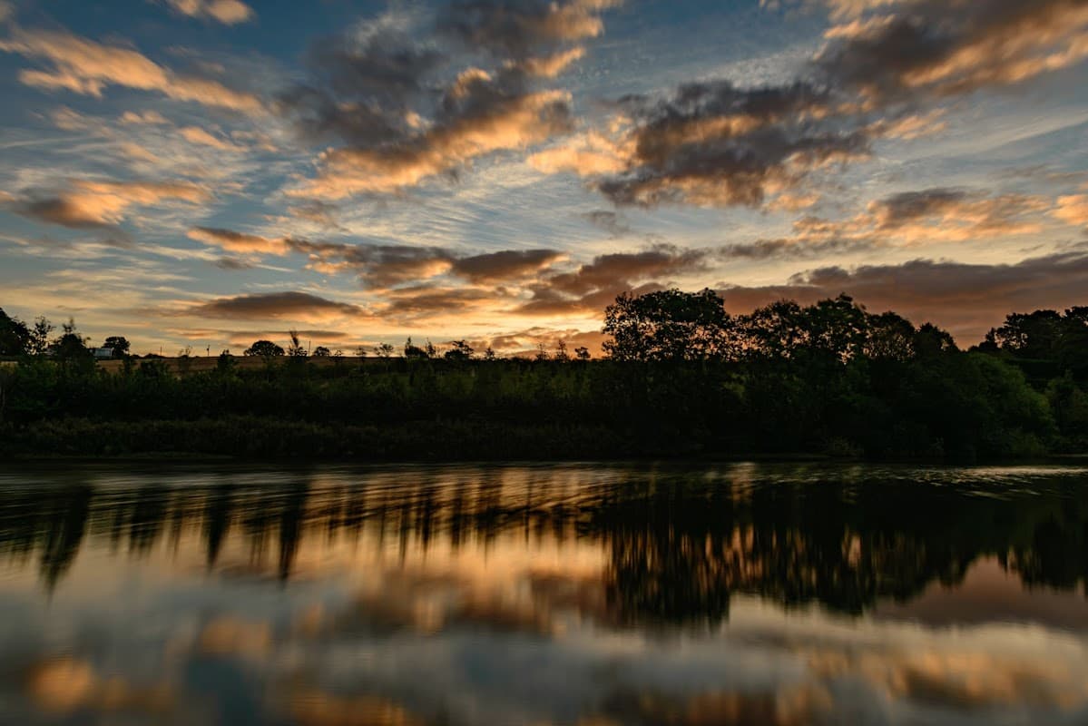 Sunset over Ulley Country Park, reflecting on calm water, with trees silhouetted against a colorful sky.