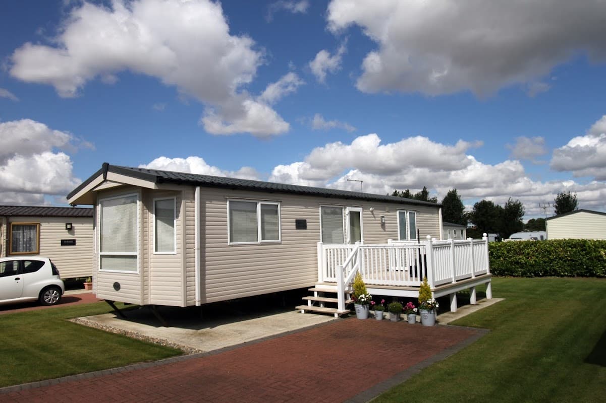 Caravan with a deck and potted plants, set against a blue sky with fluffy clouds at Four Acres Caravan Park.