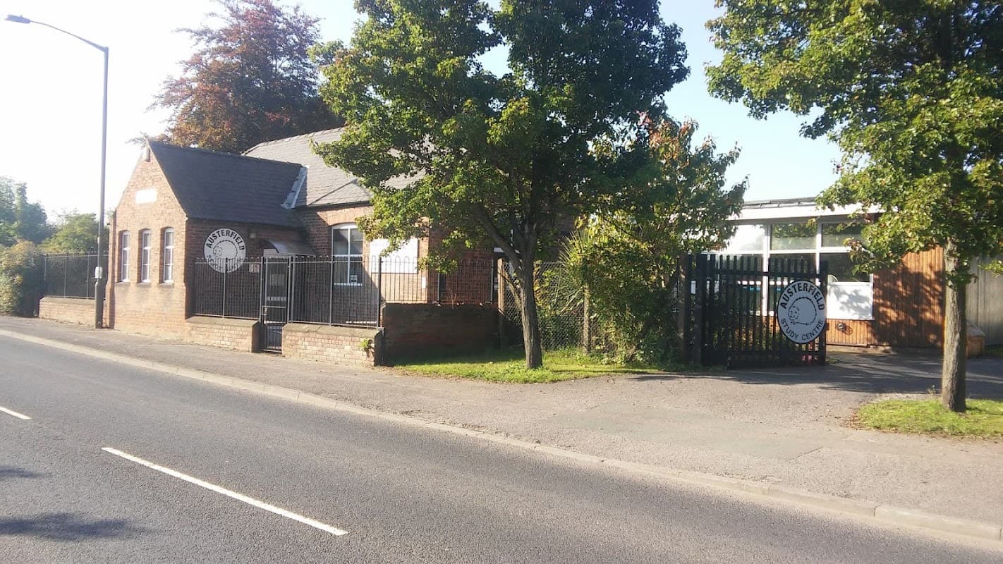 Austerfield Study Centre building with trees, a gated entrance, and a clear blue sky. Roadside view in Yorkshire.