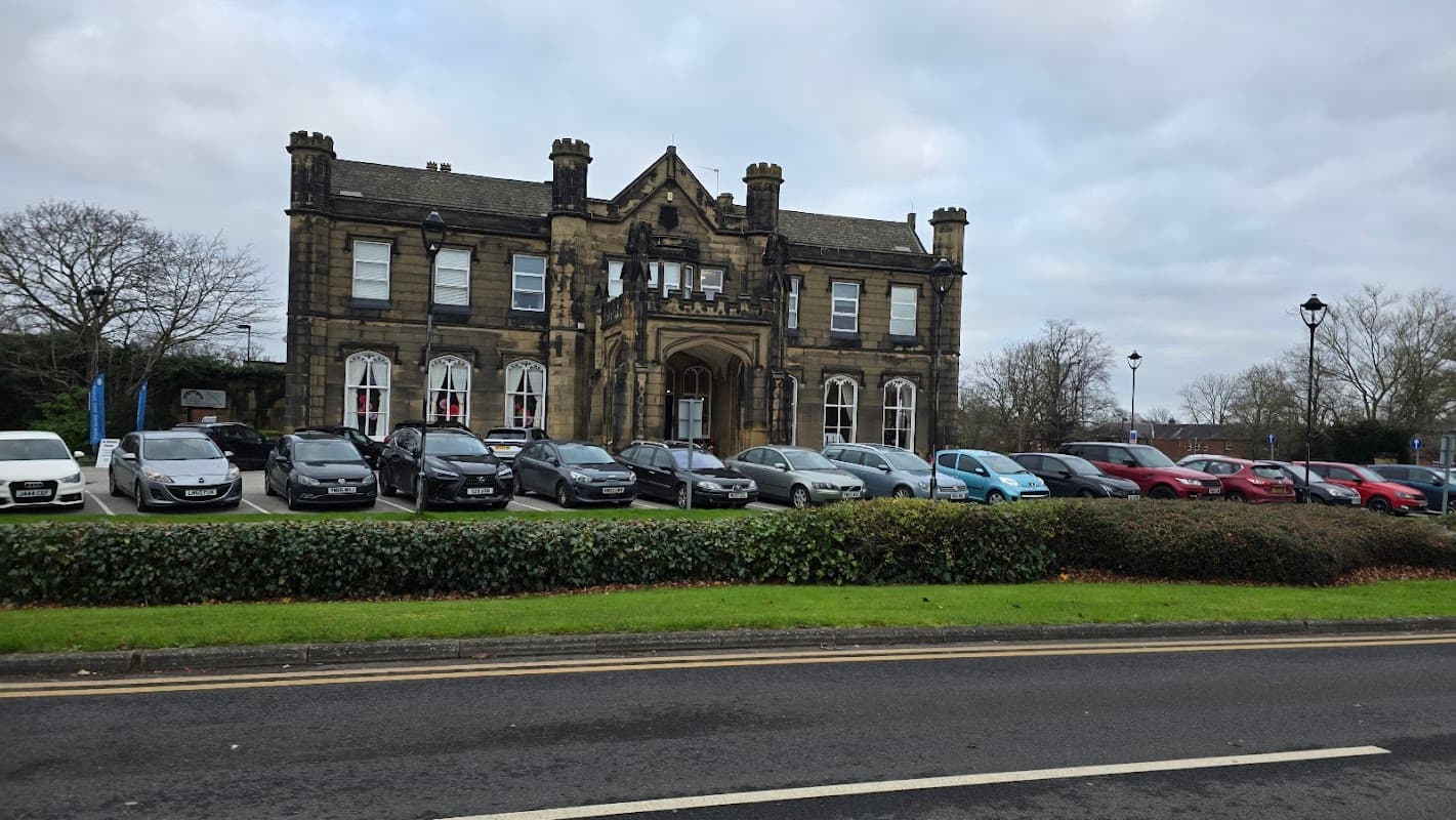 Victorian-style community hall with stone faΓ§ade, large windows, and a landscaped front lawn, surrounded by parked cars.
