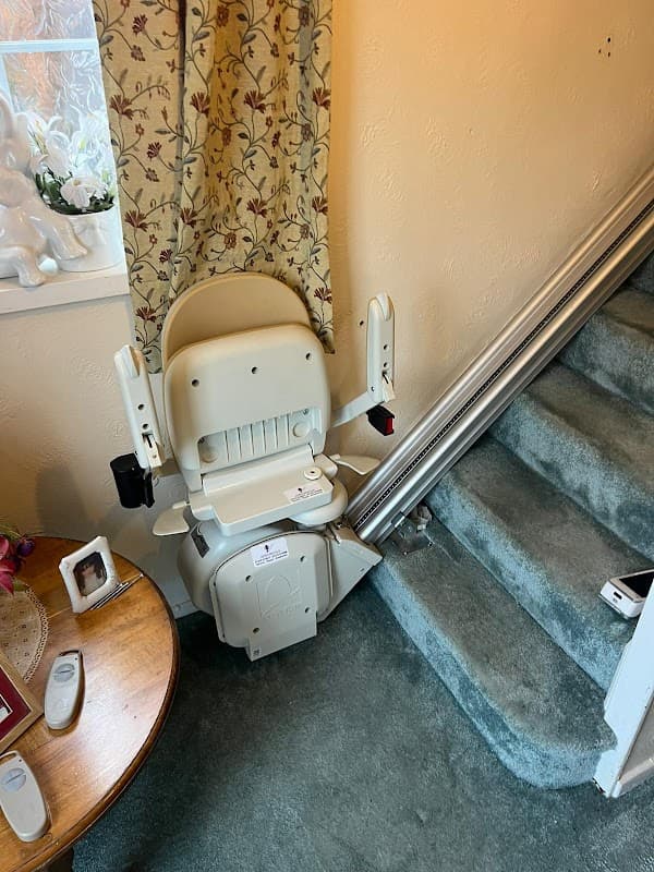 Stairlift installed at the bottom of a staircase, with a table and decorative curtains in the background.