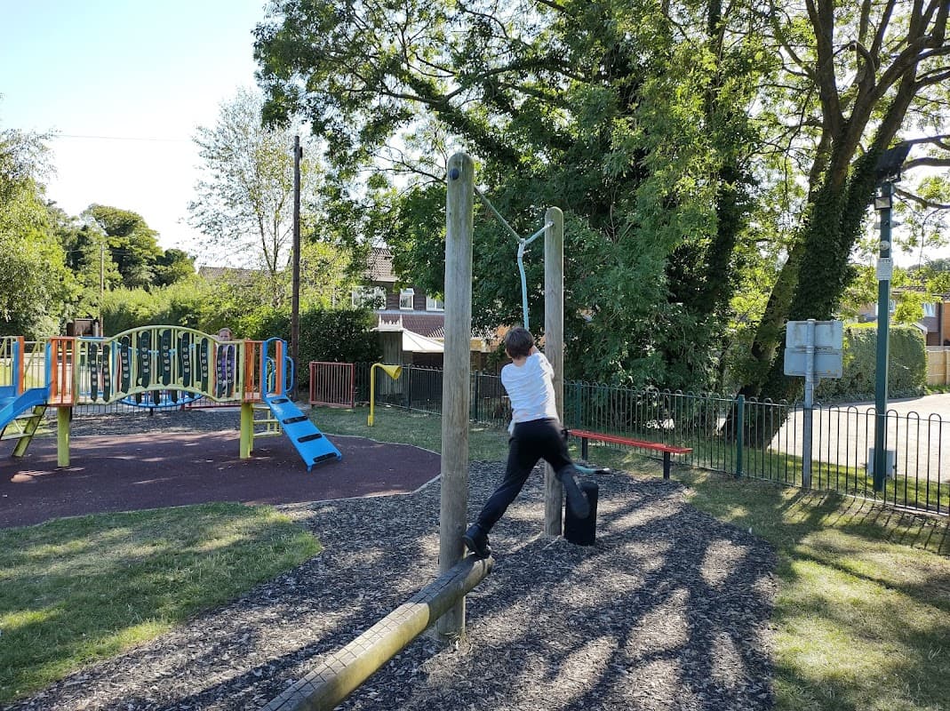 Child playing on a horizontal bar in a playground with colorful equipment and greenery in Bardsey, Yorkshire.