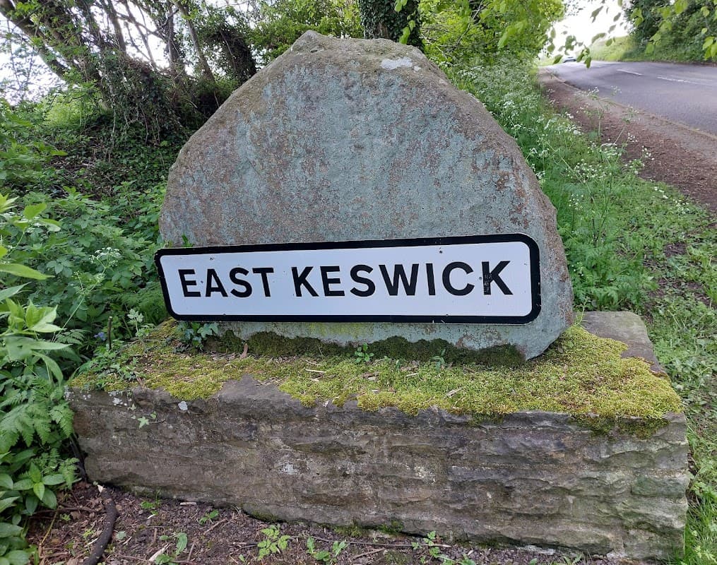 Stone sign reading "EAST KESWICK" surrounded by greenery near a road in Bardsey, Yorkshire.