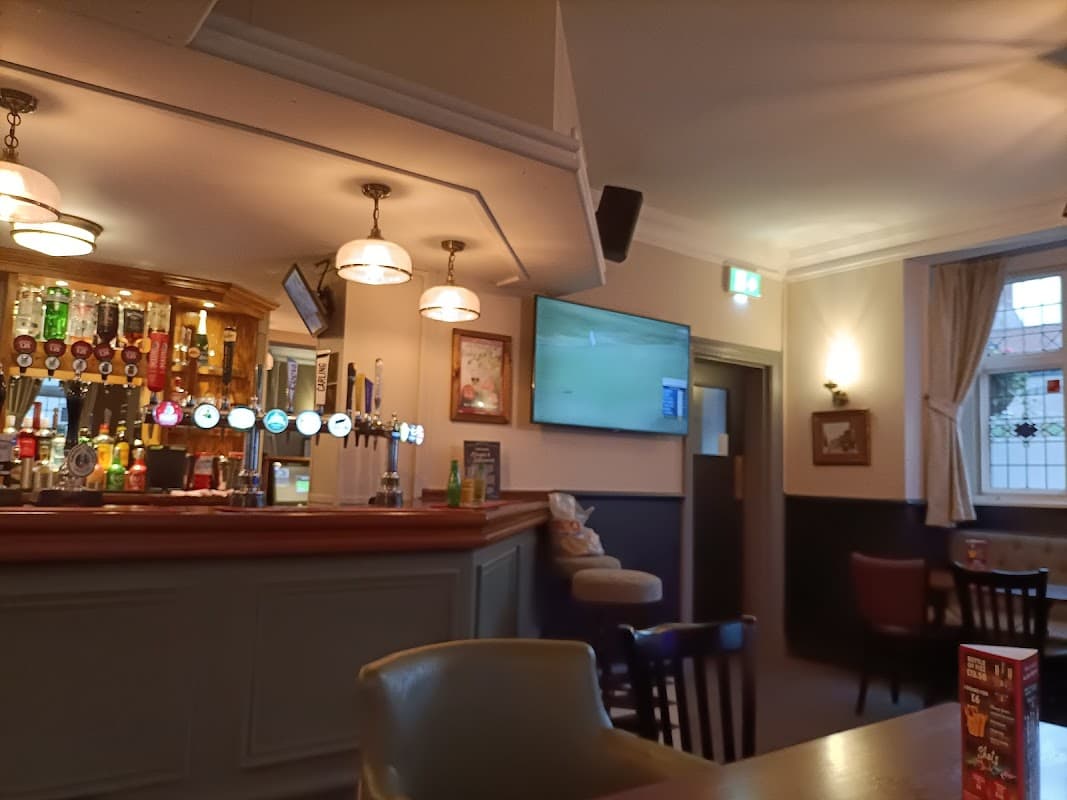 Interior of a cozy bar with a wooden counter, beer taps, a TV screen, and seating areas.