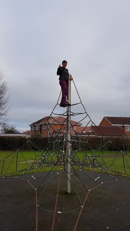 Child standing on top of a climbing structure in a playground, giving a thumbs-up, with houses in the background.