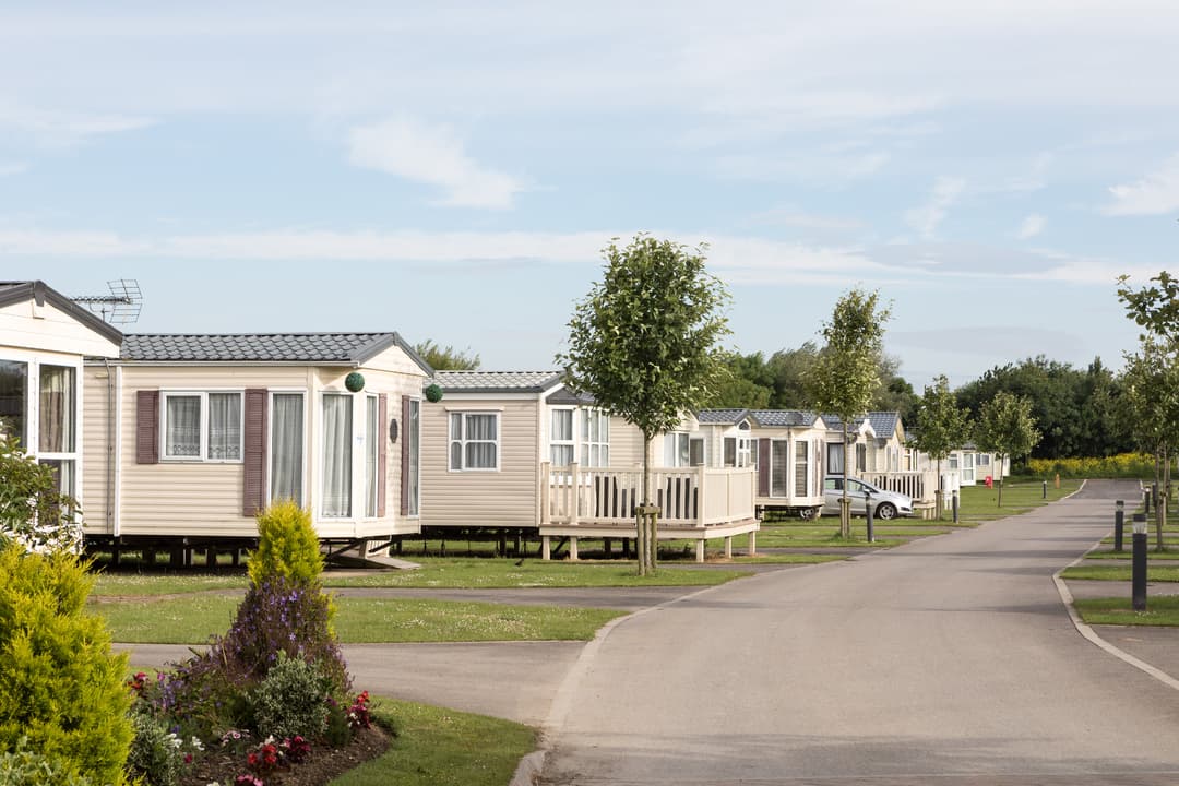 Row of holiday caravans along a paved road, surrounded by green grass and trees at Skipsea Sands Holiday Park.