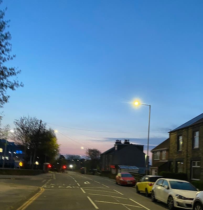 Car park with parked cars along a quiet road, streetlights illuminating a dusk sky in Barnsley, Yorkshire.