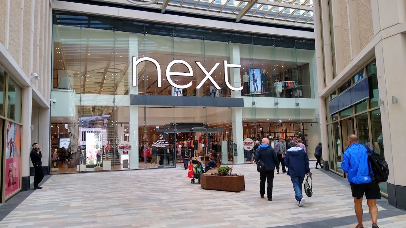 Shoppers walk towards the Next store entrance in Barnsley Markets, featuring large glass windows and modern architecture.