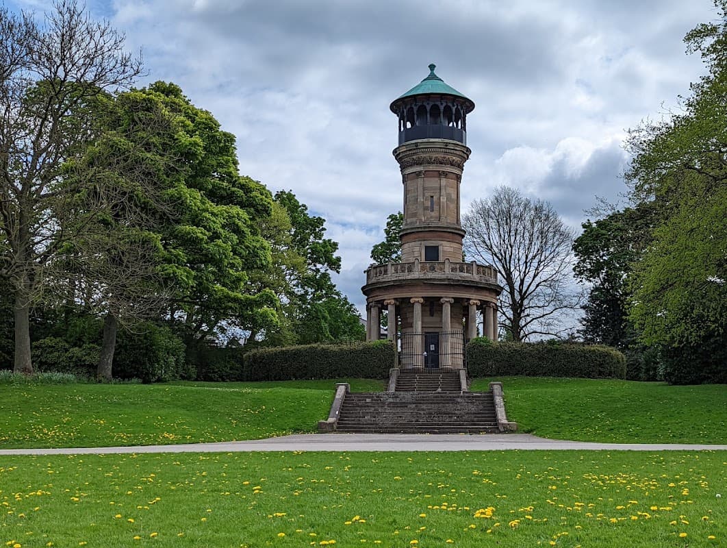 Victorian tower surrounded by lush green grass and trees under a cloudy sky at Locke Park, Barnsley.