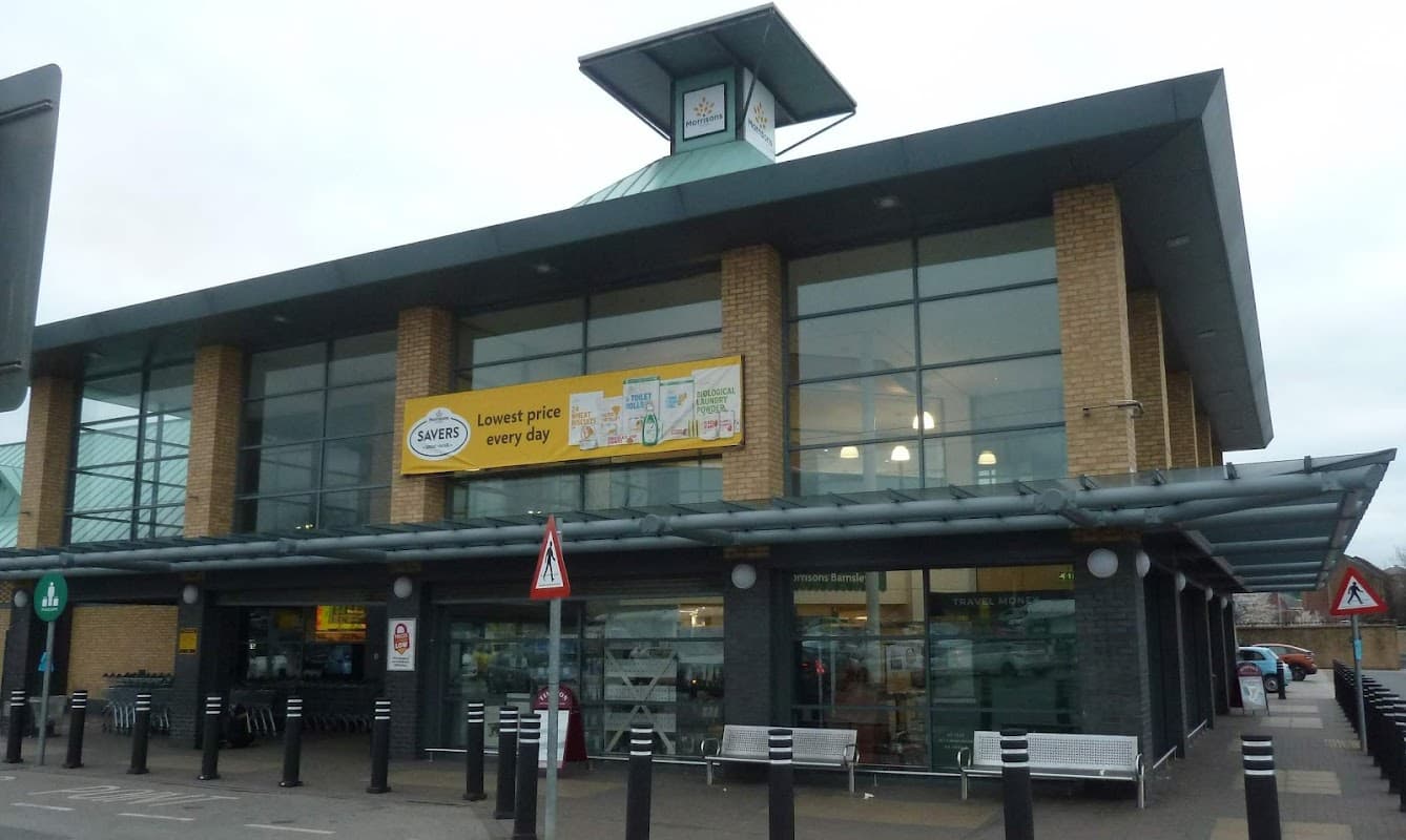 Morrisons supermarket in Barnsley with large glass windows and a prominent yellow banner advertising low prices.
