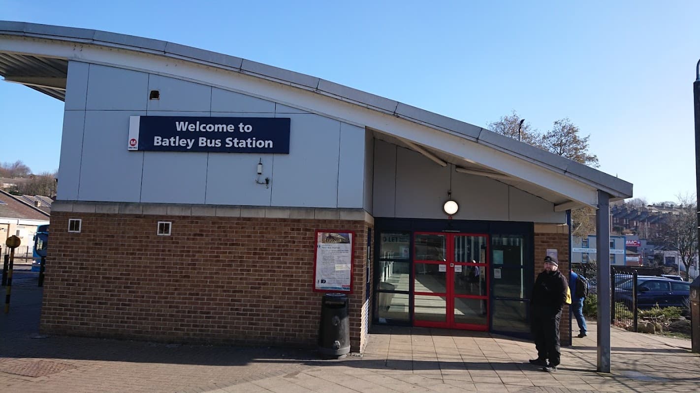 Welcome sign for Batley Bus Station, modern architecture, red doors, and a person standing outside on a sunny day.