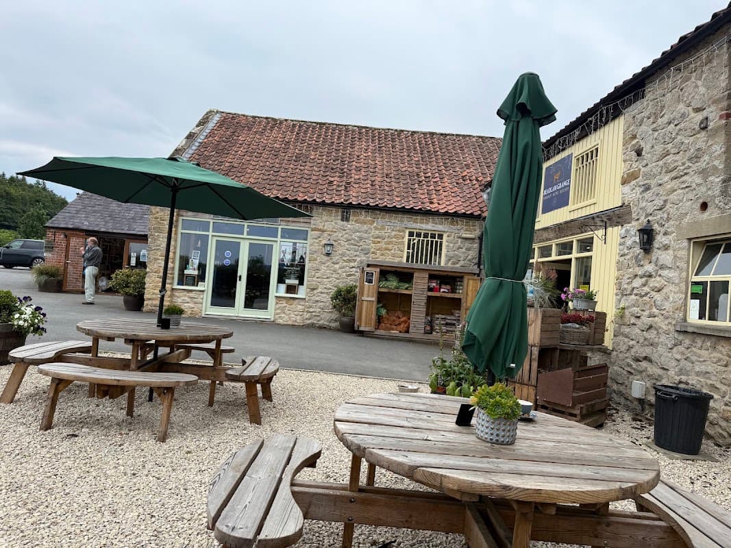 Beadlam Grange Café features outdoor seating with wooden tables, green umbrellas, and a stone building backdrop.