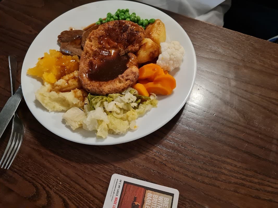A plate of traditional roast dinner with Yorkshire pudding, vegetables, and gravy on a wooden table.