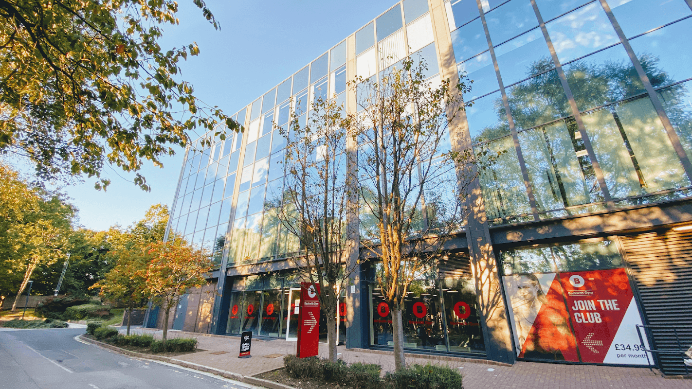Modern glass building of Beckwith Health Club with trees and signage promoting membership.