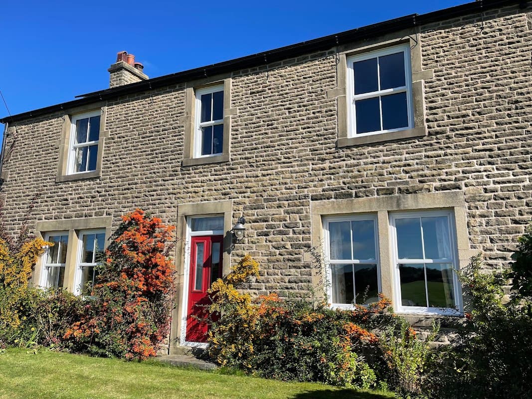 Stone cottage with red door, surrounded by colorful flowers and greenery, under a clear blue sky in Yorkshire.
