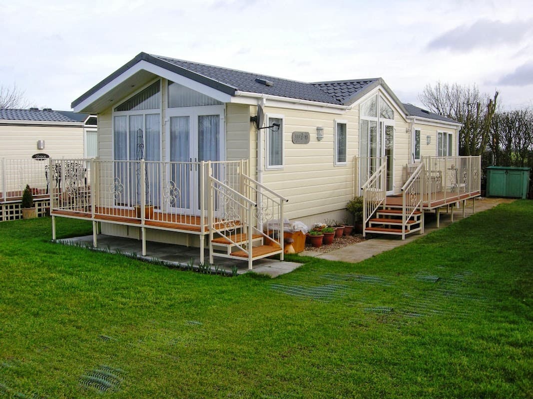 Modern holiday home with a light exterior, wooden deck, and garden area, set in a green landscape at Hawthorns Holiday Park.