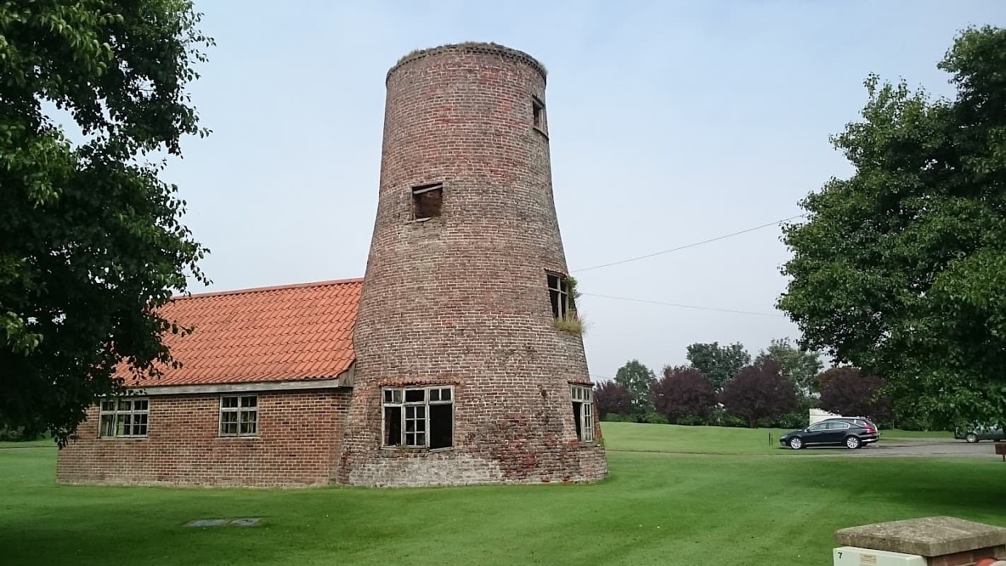 Historic brick building with a round tower, green lawn, and trees, set in a tranquil landscape in Bempton, Yorkshire.
