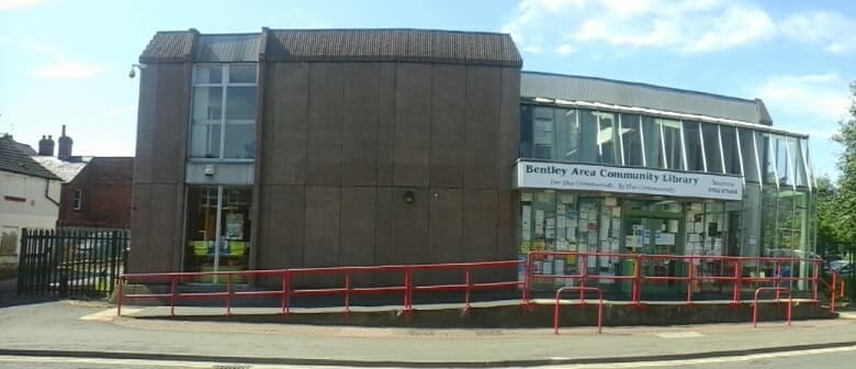 Bentley Area Community Library building with large windows, red railings, and community notices on display.