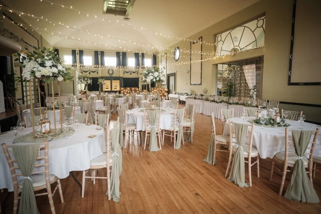 Elegant event space featuring round tables with white linens, greenery centerpieces, and twinkling string lights.