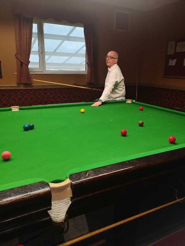 A man in a white shirt stands at a snooker table with colorful balls arranged on a green felt surface.