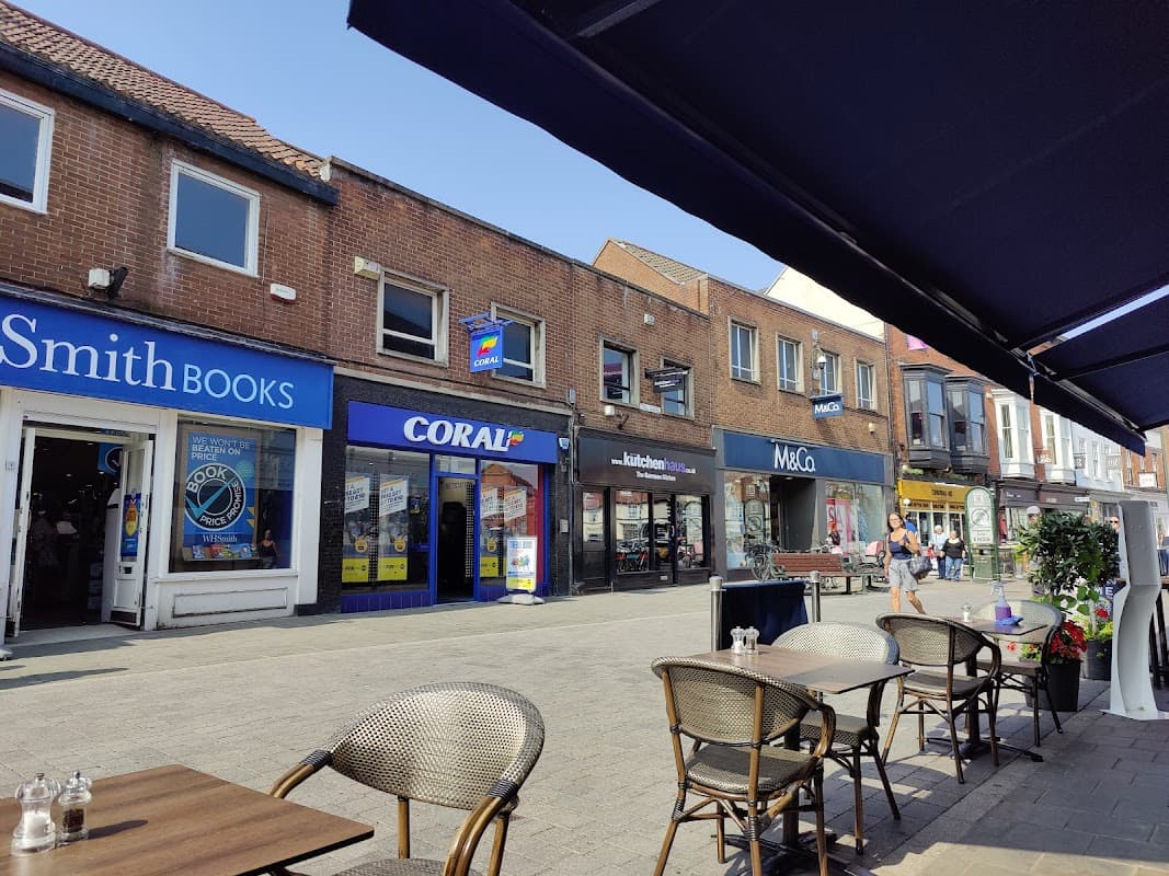 Shops line a sunny street in Beverley, with outdoor seating and people walking by.