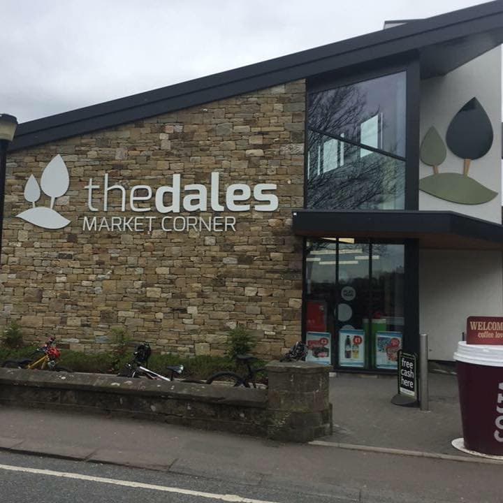 Modern stone building with large windows, featuring "the dales MARKET CORNER" signage and bicycles parked outside.