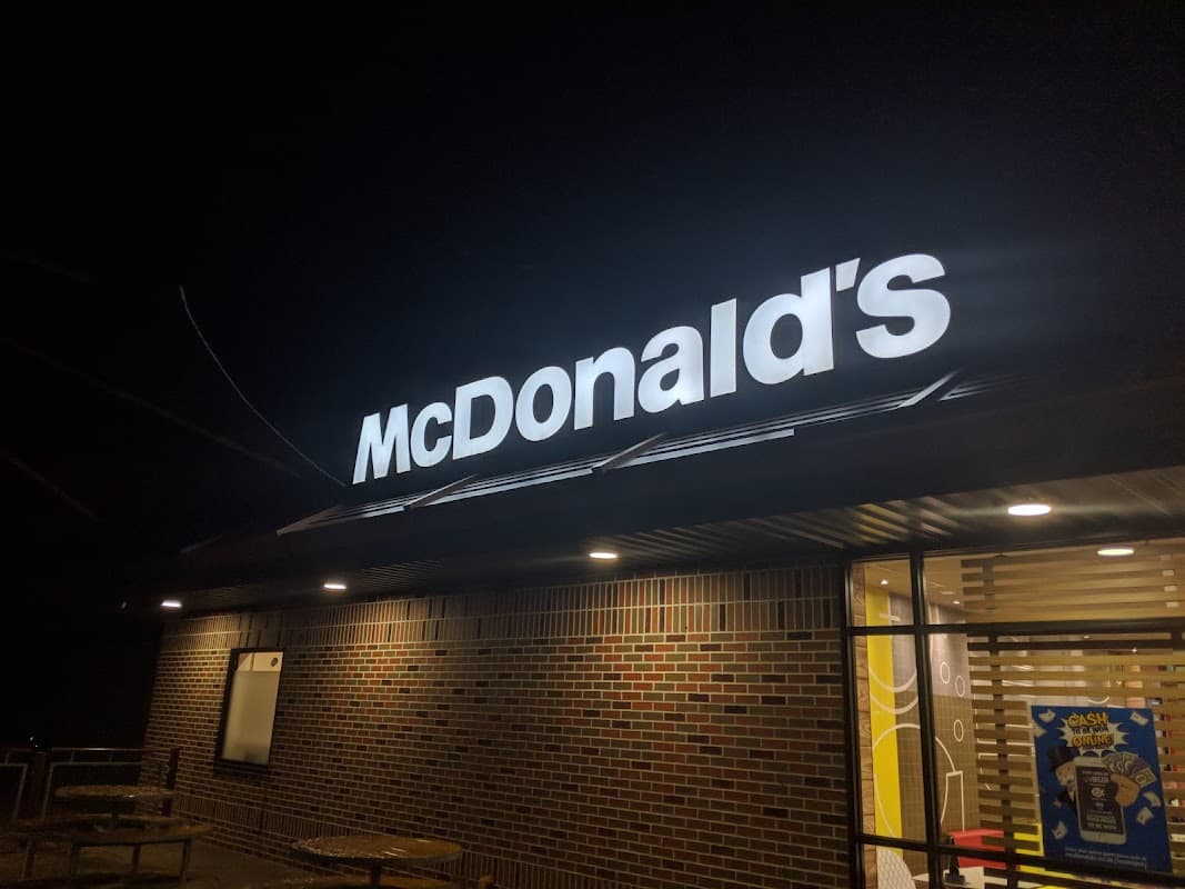 McDonald's sign illuminated at night, with brick facade and large windows showcasing the cafe's interior.