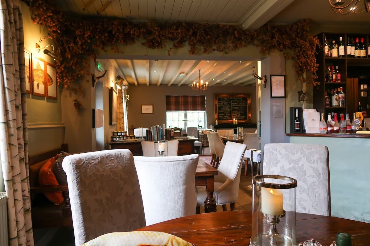 Cozy bar interior with wooden tables, chairs, and a well-stocked counter, adorned with warm lighting and decorative foliage.