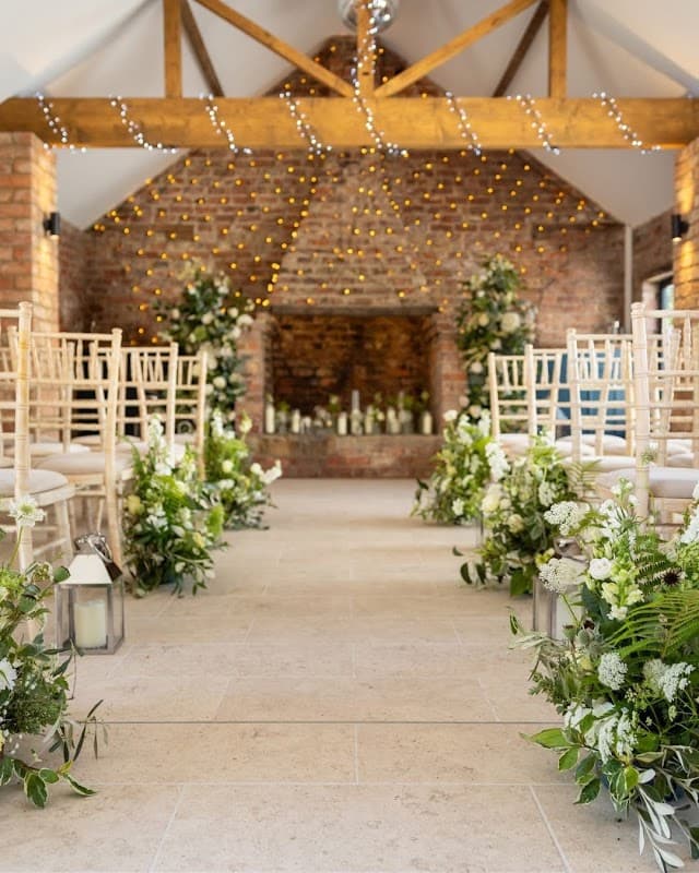 Rustic wedding venue with wooden beams, fairy lights, floral arrangements, and elegant chairs along a stone pathway.