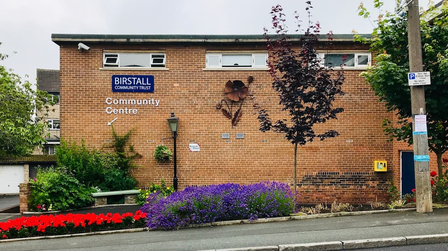 Birstall Community Centre with brick exterior, colorful flower beds, and a decorative wall feature.