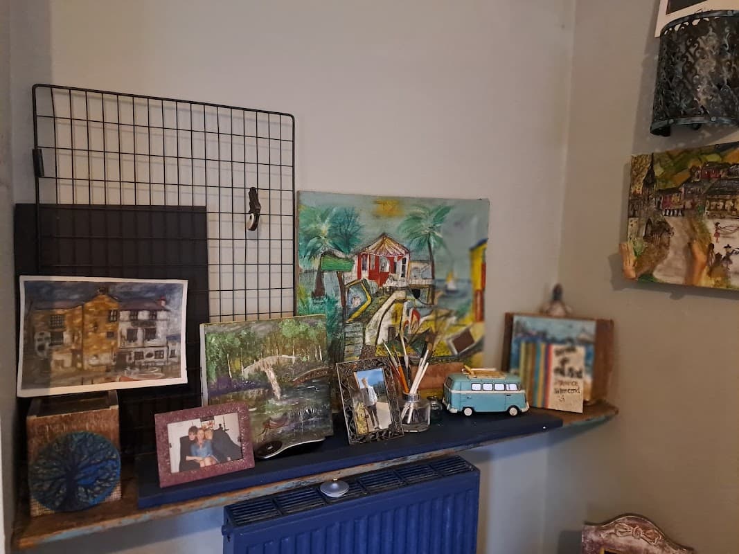 Colorful artwork and framed photos displayed on a shelf, with a blue radiator beneath in a cozy interior setting.