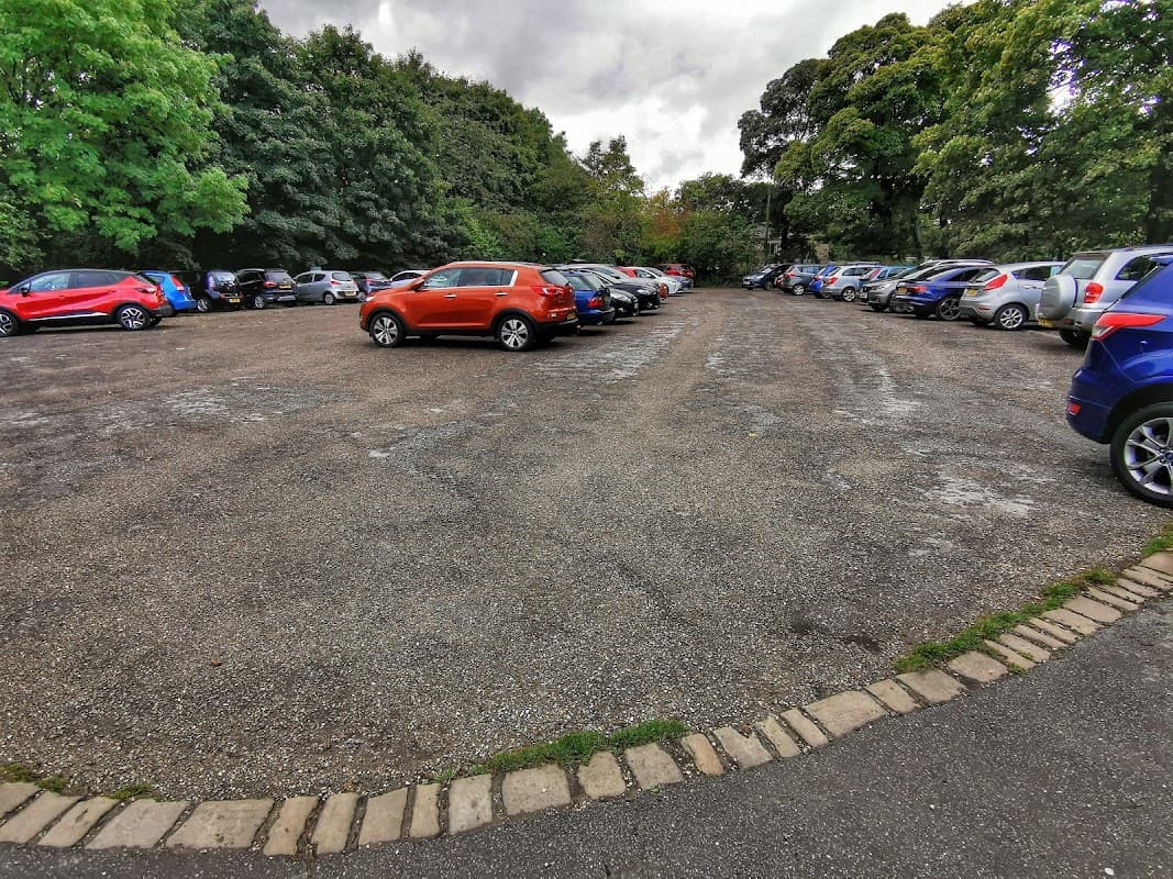 Free parking lot at Warrens Ln, Birstall, with various parked cars and trees lining the background.