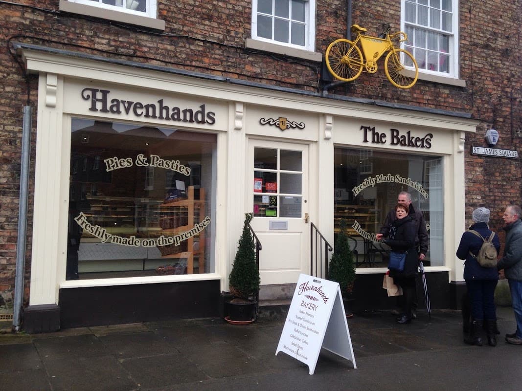 Havenhands The Bakers storefront with yellow bicycle decor, menu signage, and customers outside in Boroughbridge, Yorkshire.