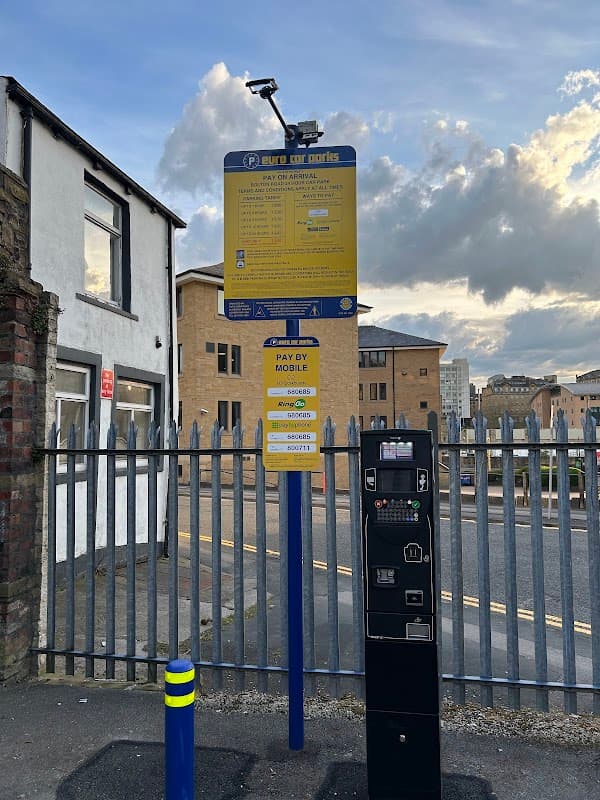 Pay & Display parking sign and payment machine at Bolton Road Car Park, with buildings and a cloudy sky in the background.