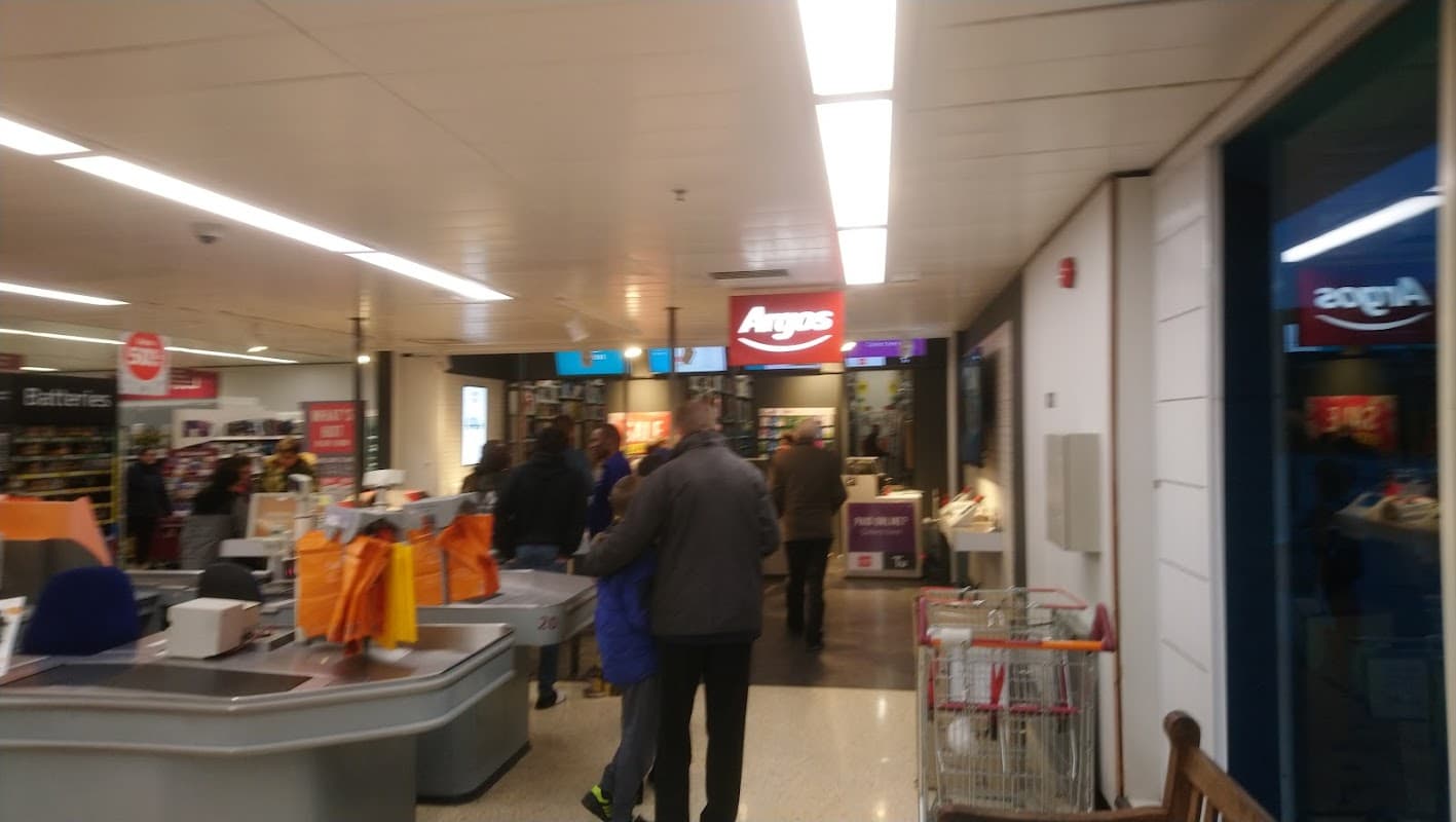 Interior of a Sainsbury's store featuring an Argos section, shopping carts, and customers browsing.