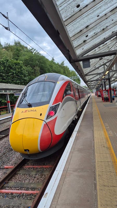 A sleek Azuma train at Bradford Forster Square Station, with green trees in the background and a covered platform.