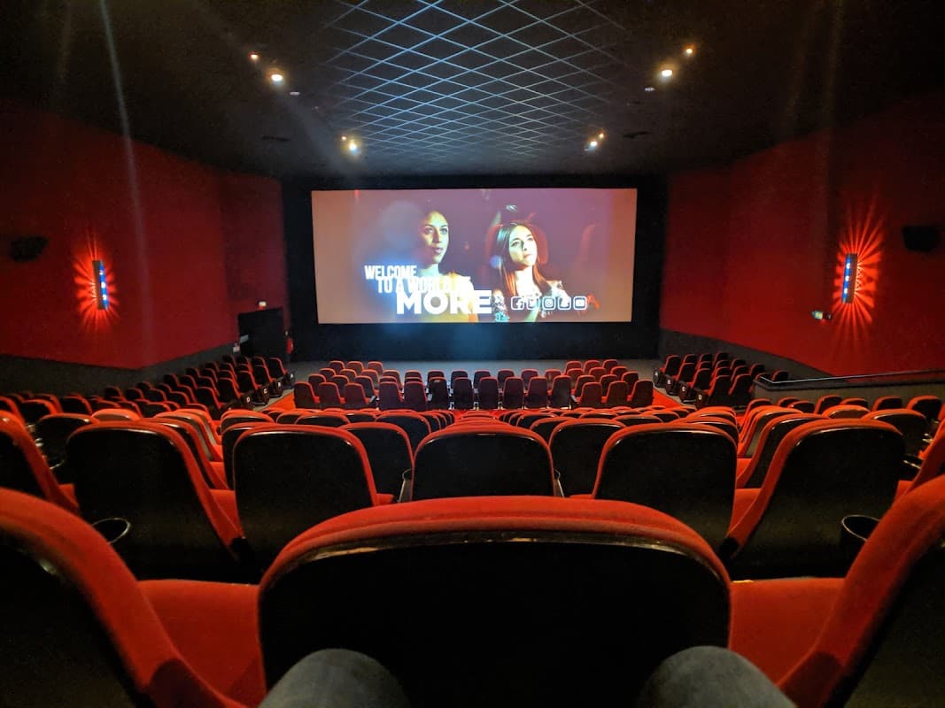 Interior of a cinema with red seating and a large screen displaying a film, creating a cozy atmosphere.