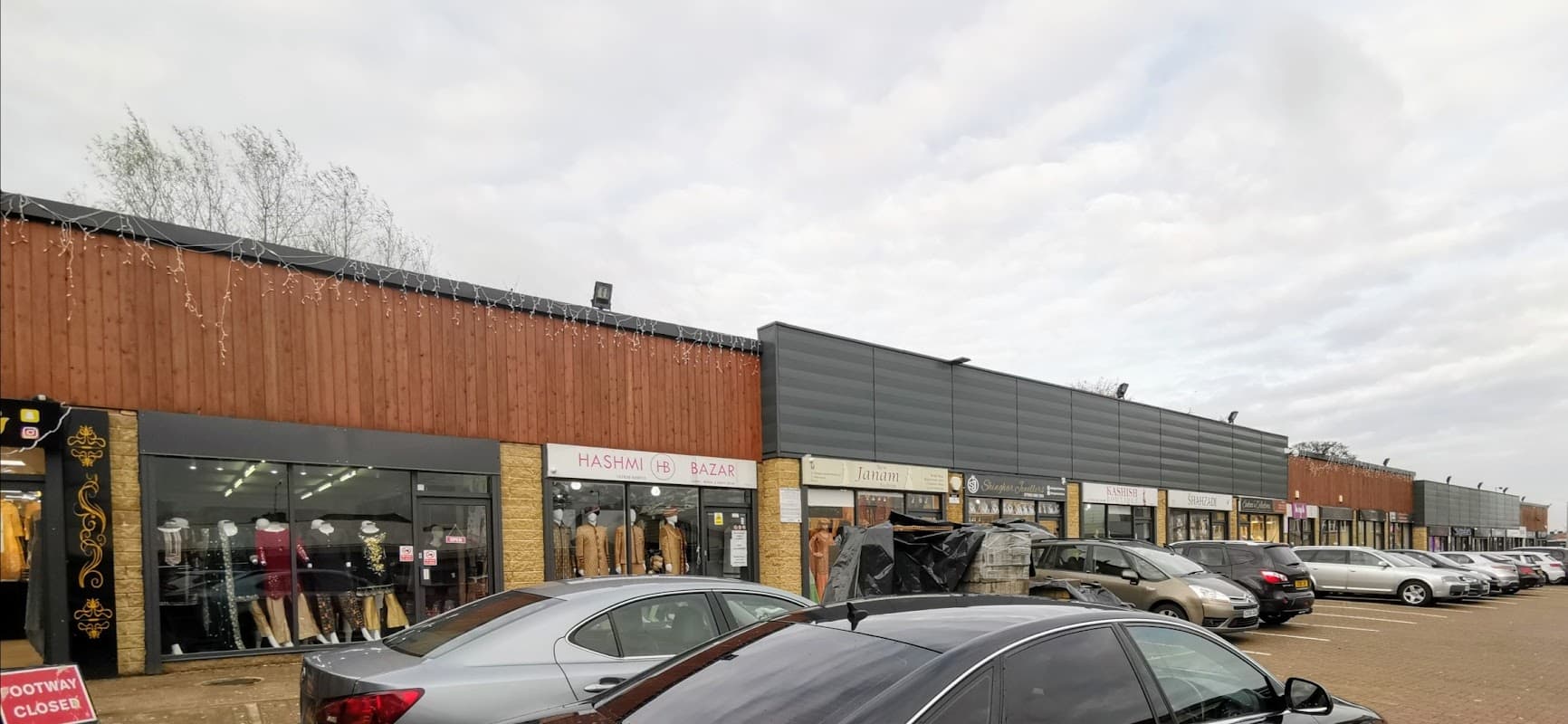 Shopping center exterior with shops, parked cars, and cloudy sky in Bradford, Yorkshire.