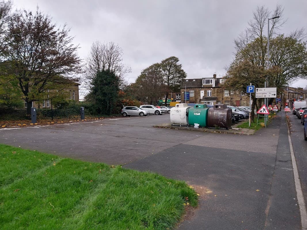 Empty car park with parked cars, green grass, and waste bins surrounded by trees and buildings in Bradford.
