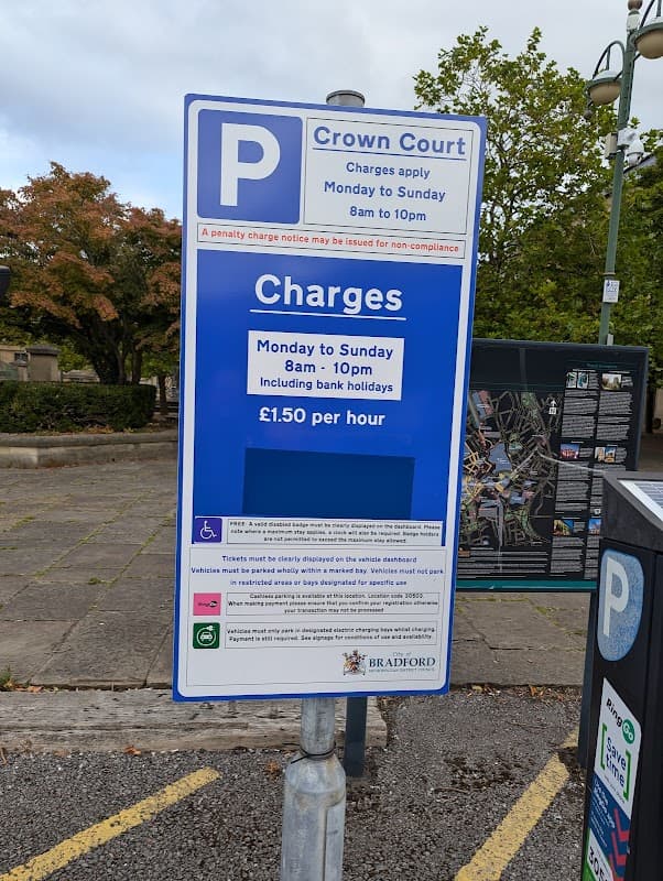 Crown Court parking sign detailing charges and hours of operation, surrounded by trees and pavement.