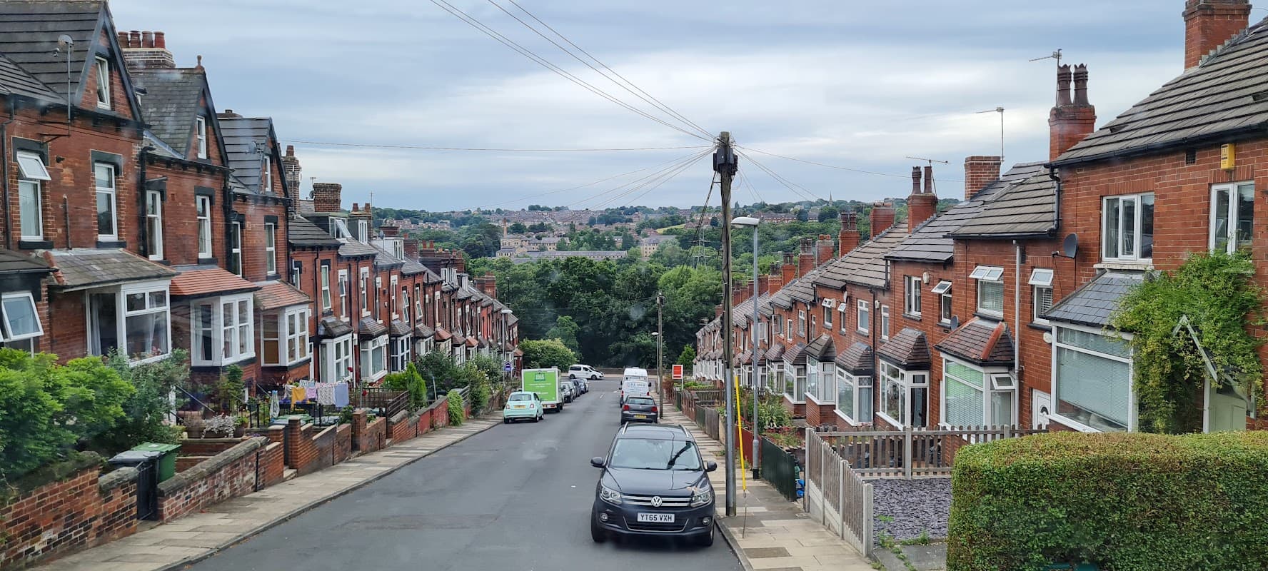Wigan St Parking in Bradford features terraced houses, parked cars, and a scenic view of greenery in the distance.