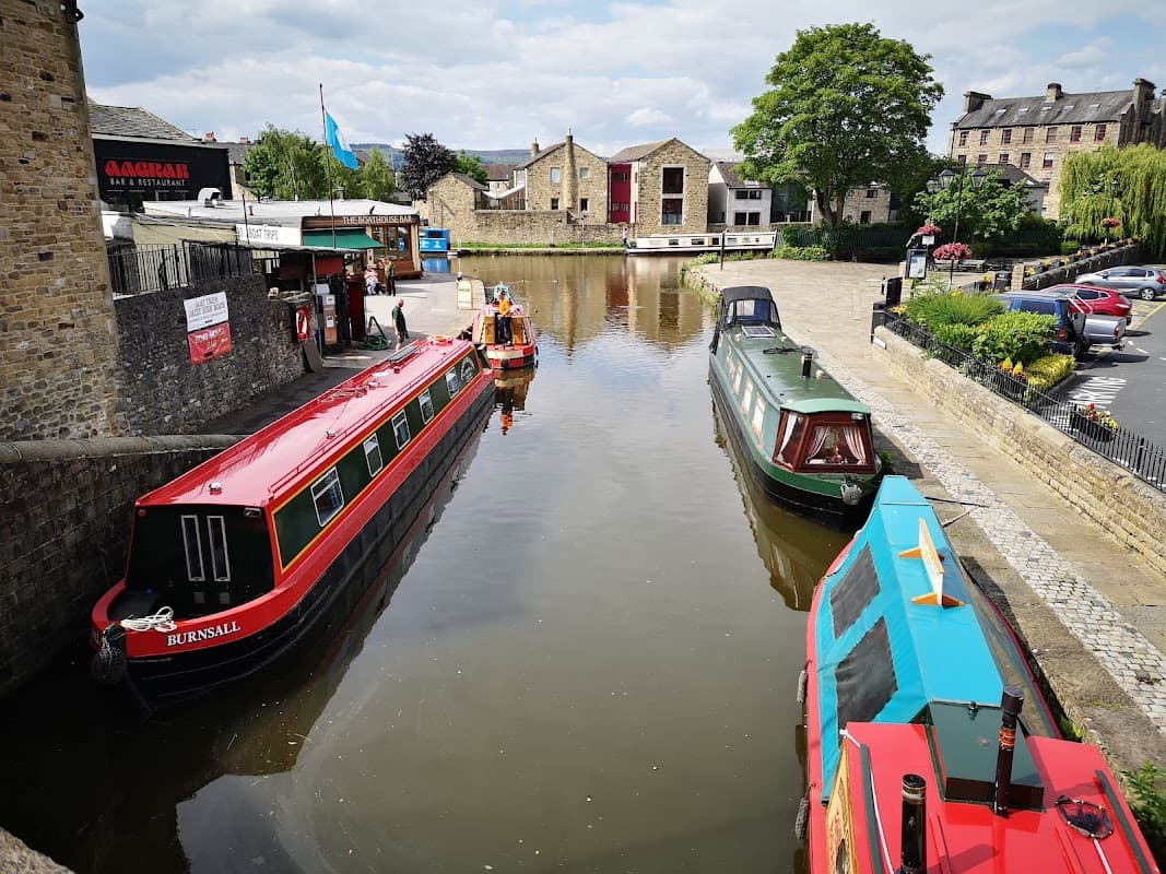 Colorful narrowboats docked along a calm waterway, with historic buildings and green trees in the background.